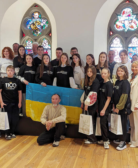 Das Foto zeigt die 30-köpfige Gruppe mit ukrainischen Kindern und Jugendlichen, die schwarze oder weiße Goslar-T-Shirts tragen, Goslars Oberbürgermeisterin, Sponsoren und Organisatoren auf der Rathausdiele. In der Mitte wird die blau-gelbe ukrainische Flagge gehalten.